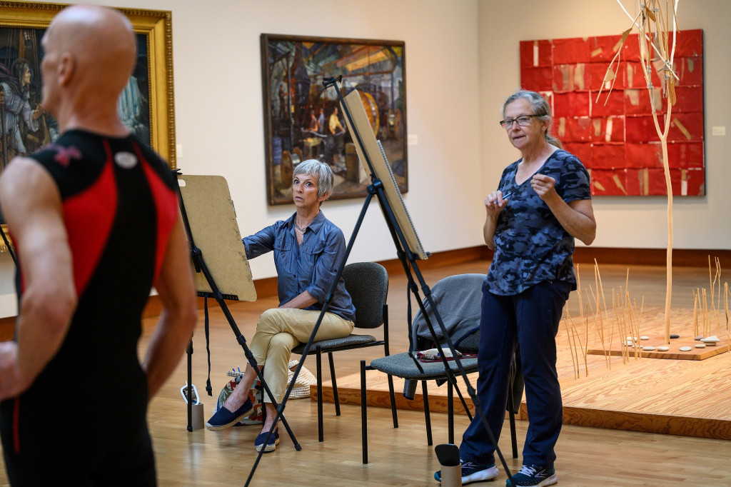Two people in an art gallery look at an easel with a drawing on it.
