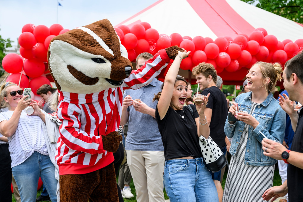 A woman twirls while holding Bucky Badger's hand.