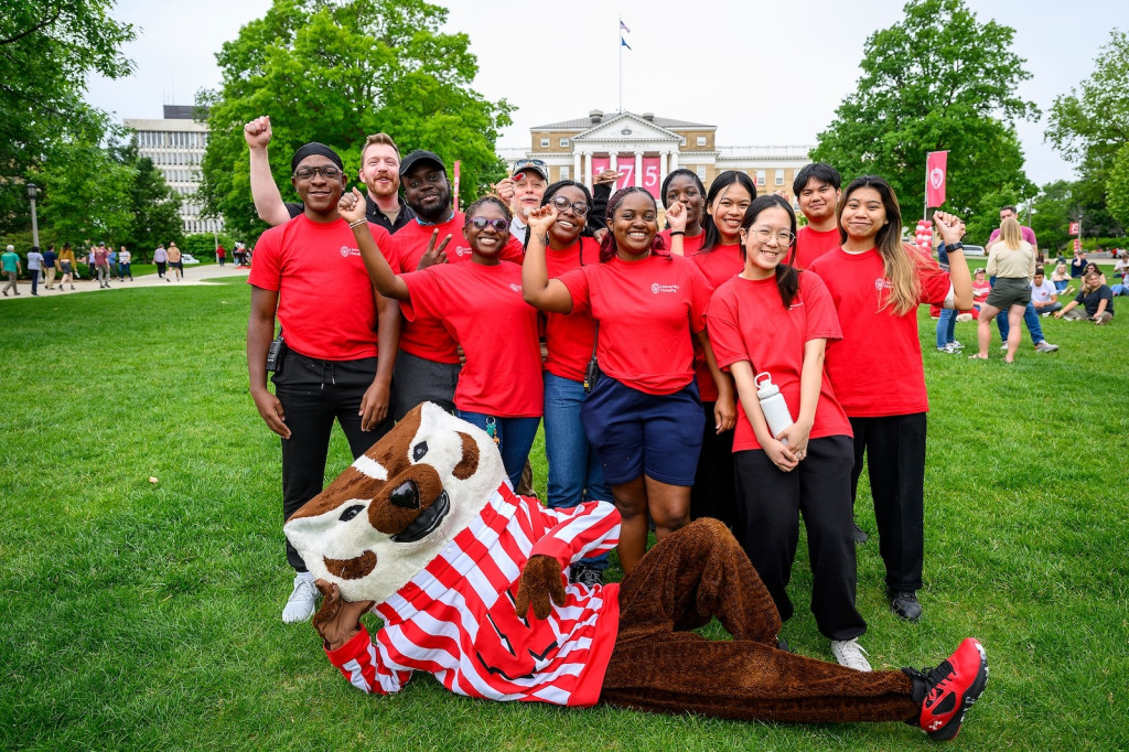 A group of people in red shirts stand and pose for the camera, along with Bucky Badger.