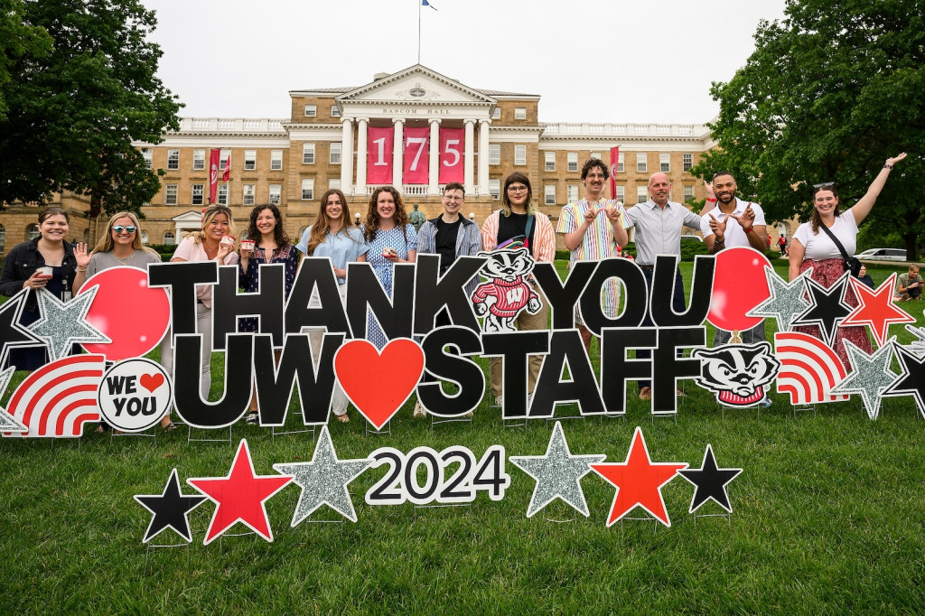 A group of people pose on a lawn with a sign reading Thank you UW staff 2024