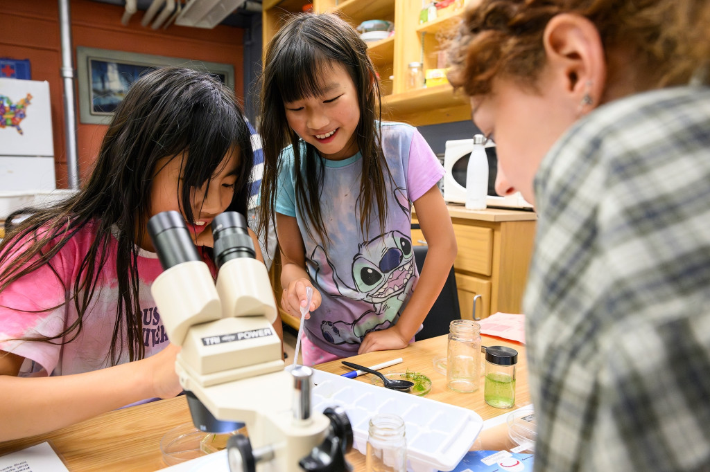Some kids look at a microscope and smile.