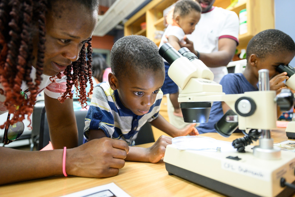 A woman and two children look into microscopes.