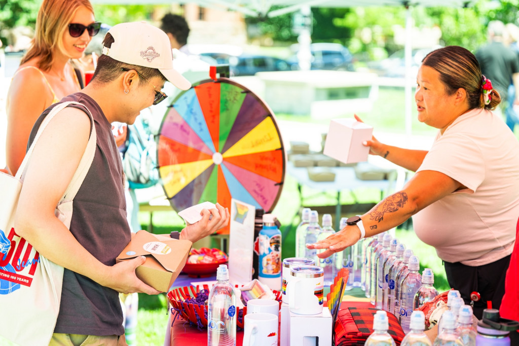 A man in front of a colorful spinning wheel hands out prizes.
