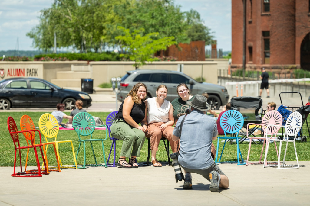 People get a photo taken while sitting in colorfully painted chairs.
