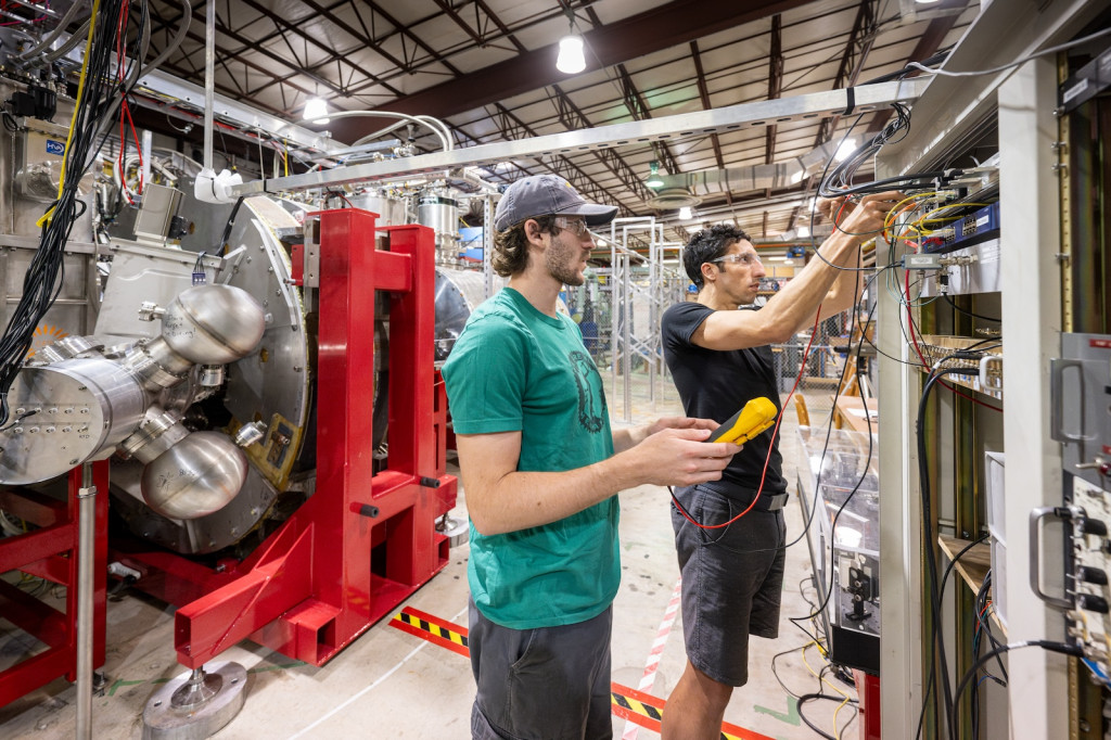 Two men adjust cords connected to a piece of heavy machinery.
