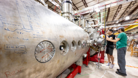 A large silvery metal cylinder is the biggest component in some machinery that people are working on.
