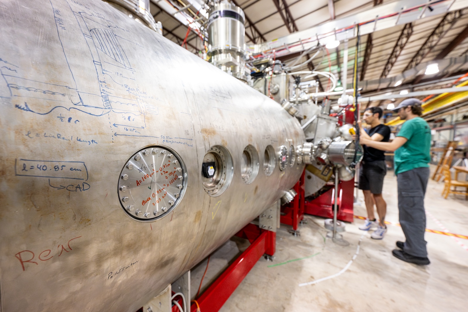 A large silvery metal cylinder is the biggest component in some machinery that people are working on.