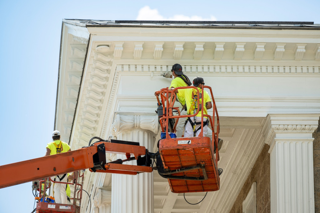 Some people standing in lifts touch up the white paint of the portico in front of Bascom Hall.