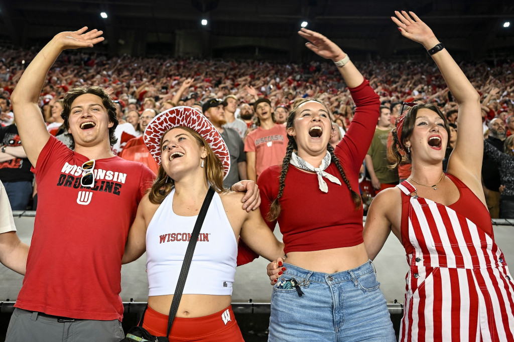 Fans hold arms around each other in stands and sing.