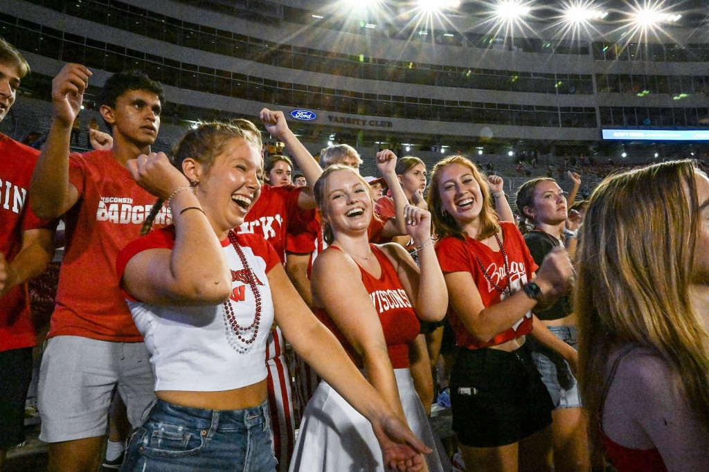 Fans wearing red Wisconsin Badger gear dance in the stands.