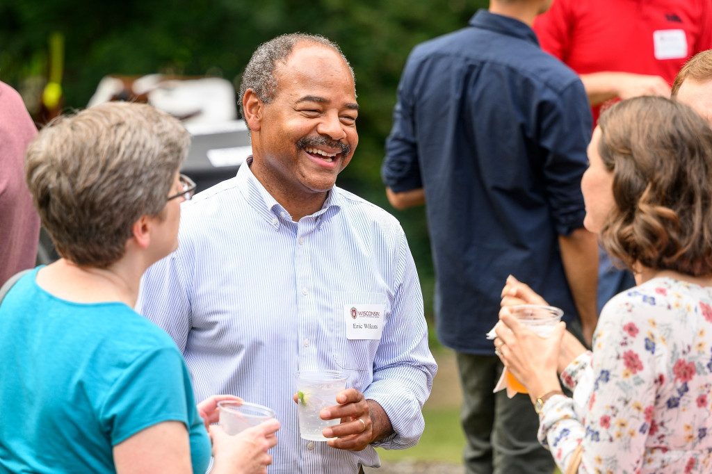 Two couples talk while holding drinks, smiling.