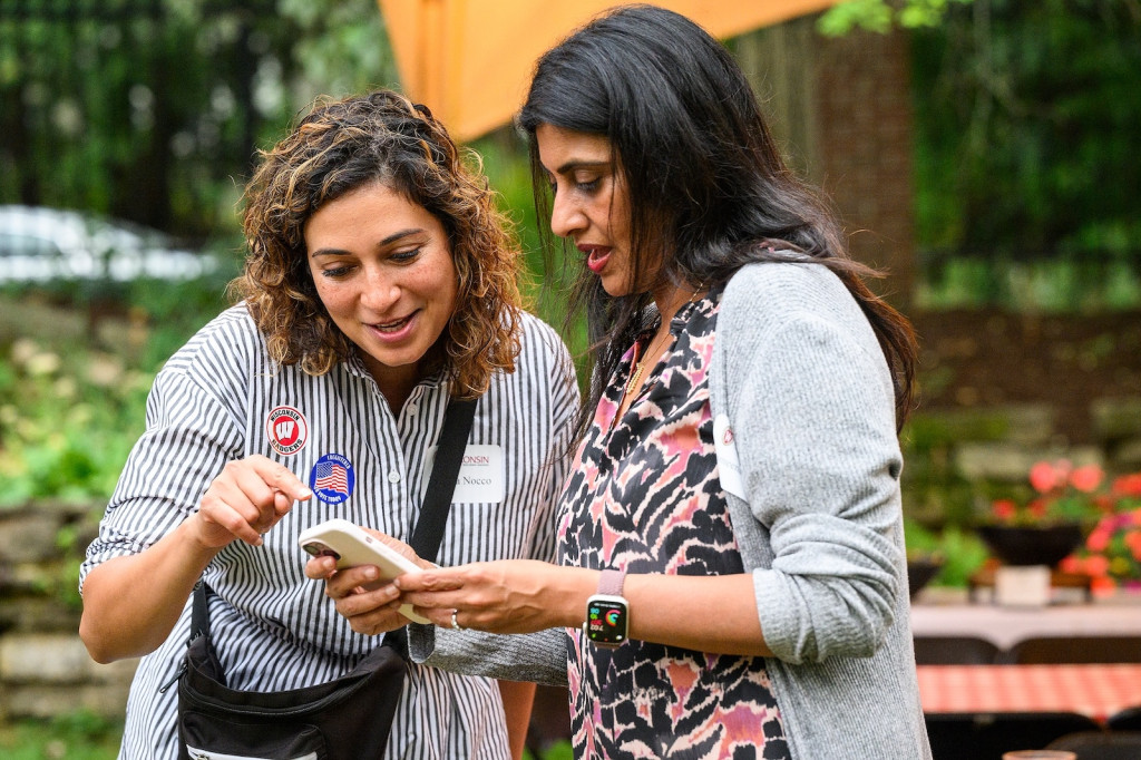 Two women huddle over a cell phone, sharing contacts.