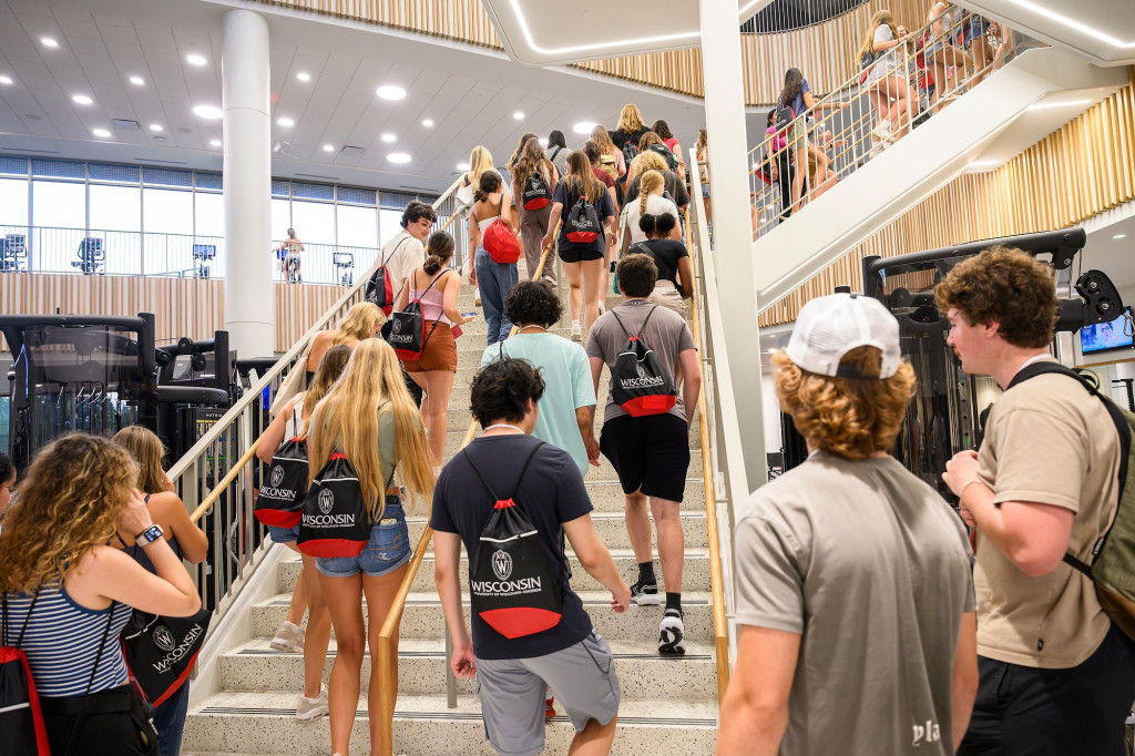 A group of students wearing backpacks walk up a flight of stairs in a new, brightly-lit building.