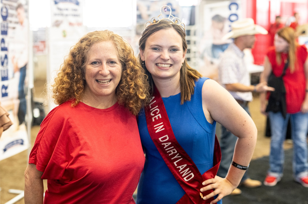 Two women stand next to each other and pose for a photos. One wears a sash and a tiara.