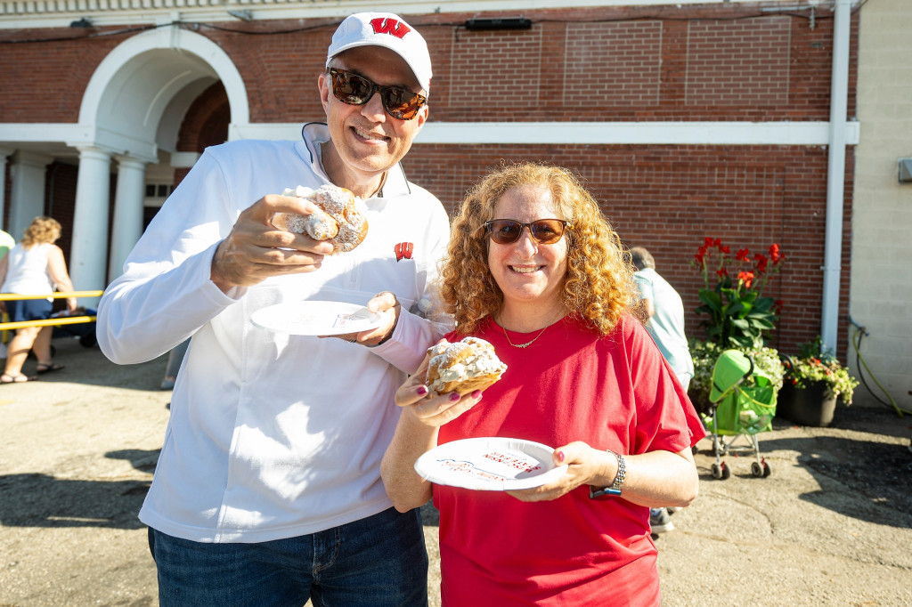 A man and a woman stand next to each other while holding a cream puff and smile at the camera.