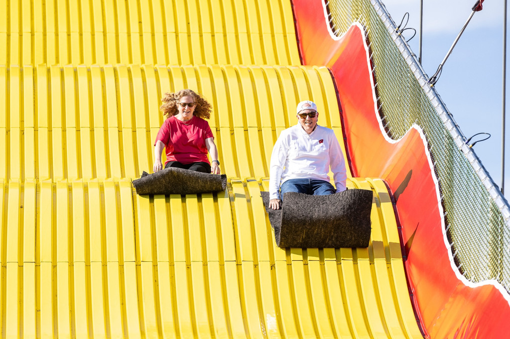 Two people happily ride down a giant slide on slippery mats.