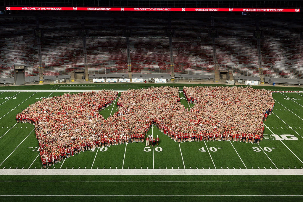 Students stand on a football field, their bodies forming a W.