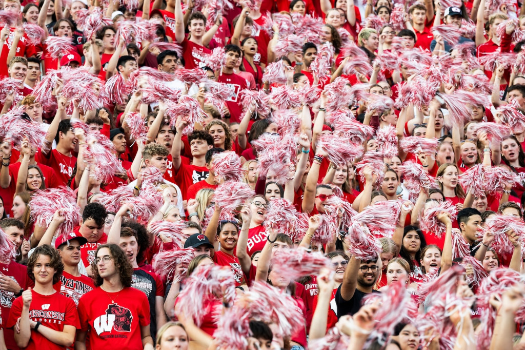 People wearing red and white Wisconsin Badger shirts cheer in stands.