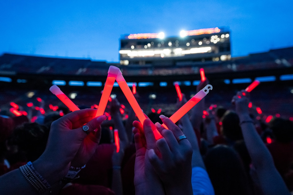 Several glow sticks are held together to form a W on the field of a stadium, which is darkening as the sun sets.