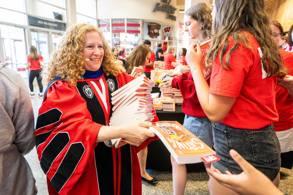 A woman hands out copies of a book.