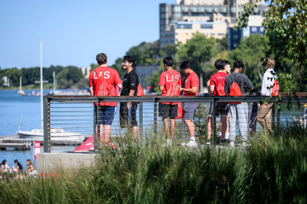 Students standing on a deck look out on the lake, as they eat ice cream.