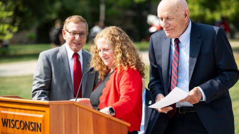 A woman and two men stand at a podium and smile and chat.