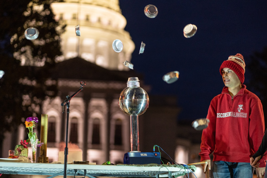 A person looks at some bubbles floating upward in the nighttime; the state capitol is lit up in the background.