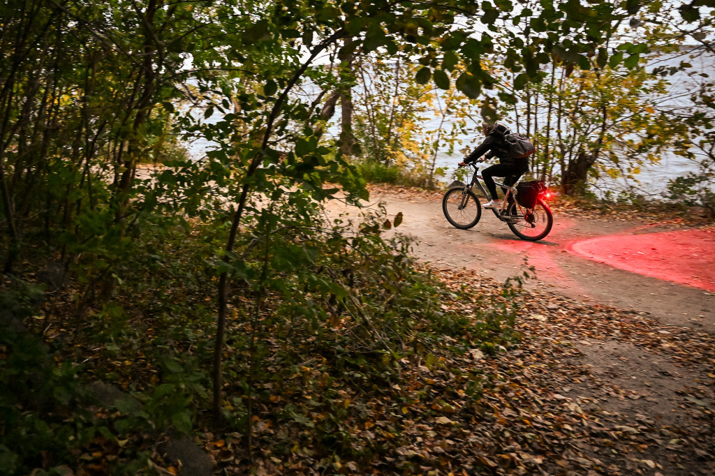 A biker is shown biking in the twilight through trees that are changing color.