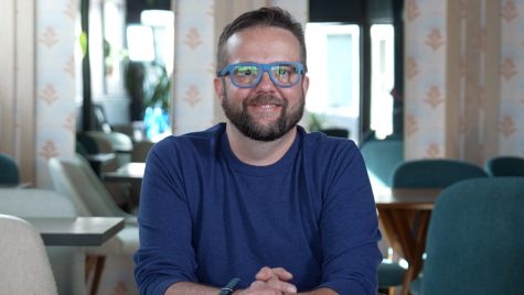 A bearded man wearing glasses smiles at the camera.