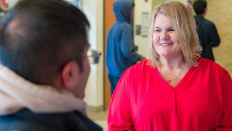 A woman in a red shirt smiles and talks to a young man.