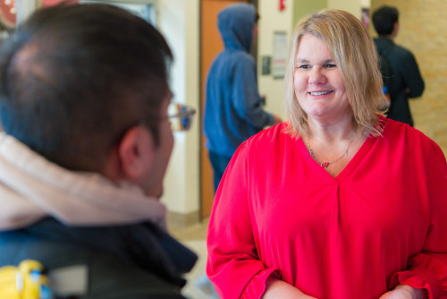 A woman in a red shirt smiles and talks to a young man.