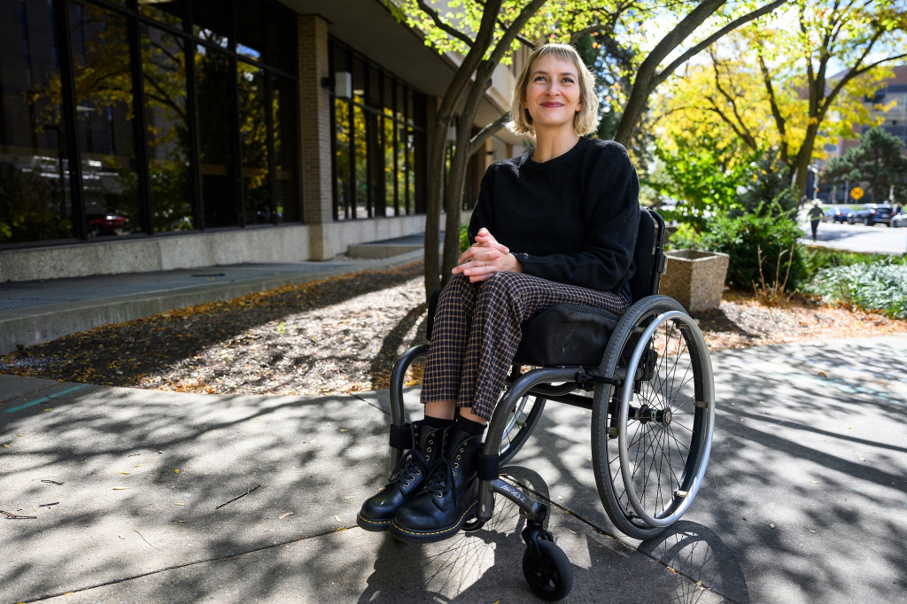 A portrait of a woman in a wheelchair on a sun-speckled plaza.