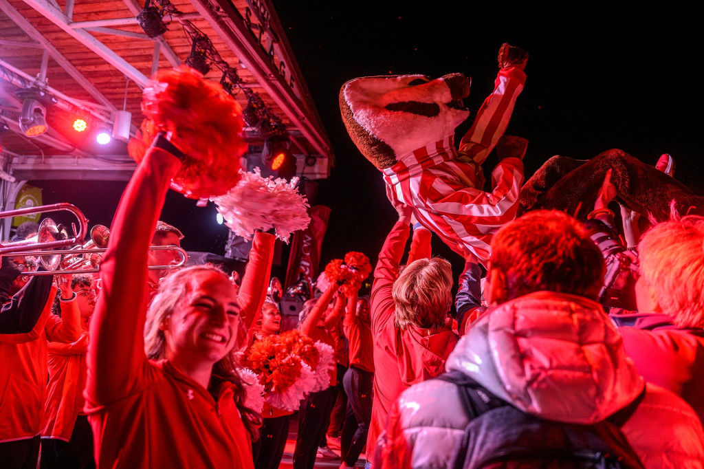 A person dressed in a Badger outfit is held up by the arms of a crowd of people.