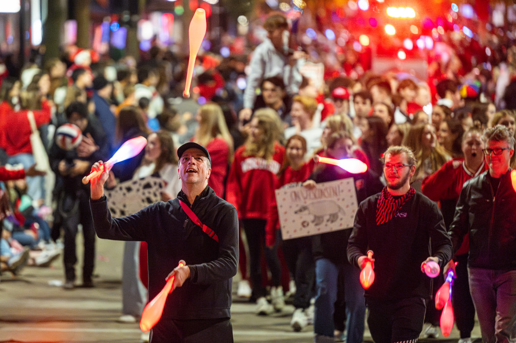 Several people juggle pins even as they walk down a street in a parade.