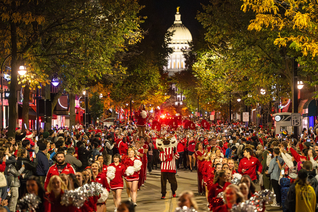 A street is crowded with spectators watching a parade progress, the state Capitol visible in the background.