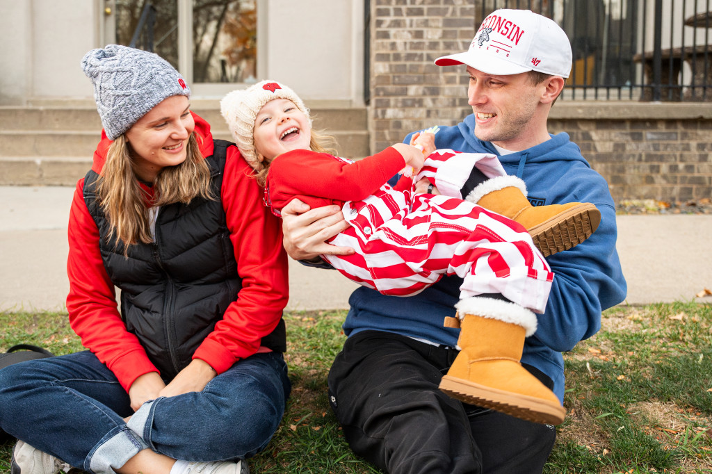 A couple and their child, all wearing red and white, play around as they wait for a parade.