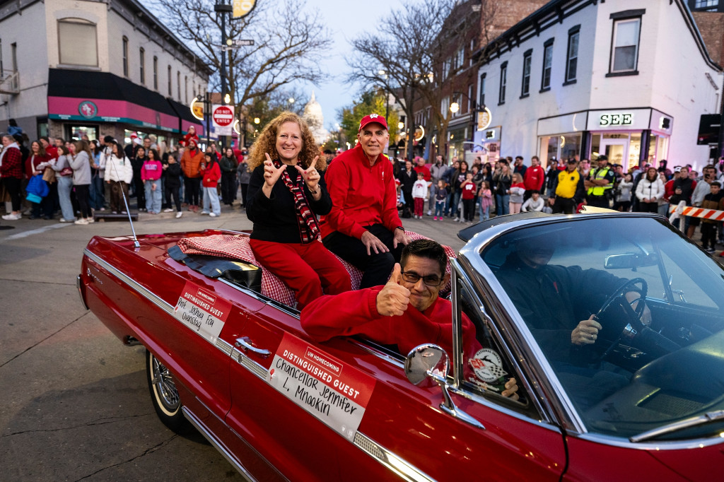 Two people in a car wave to the crowd.