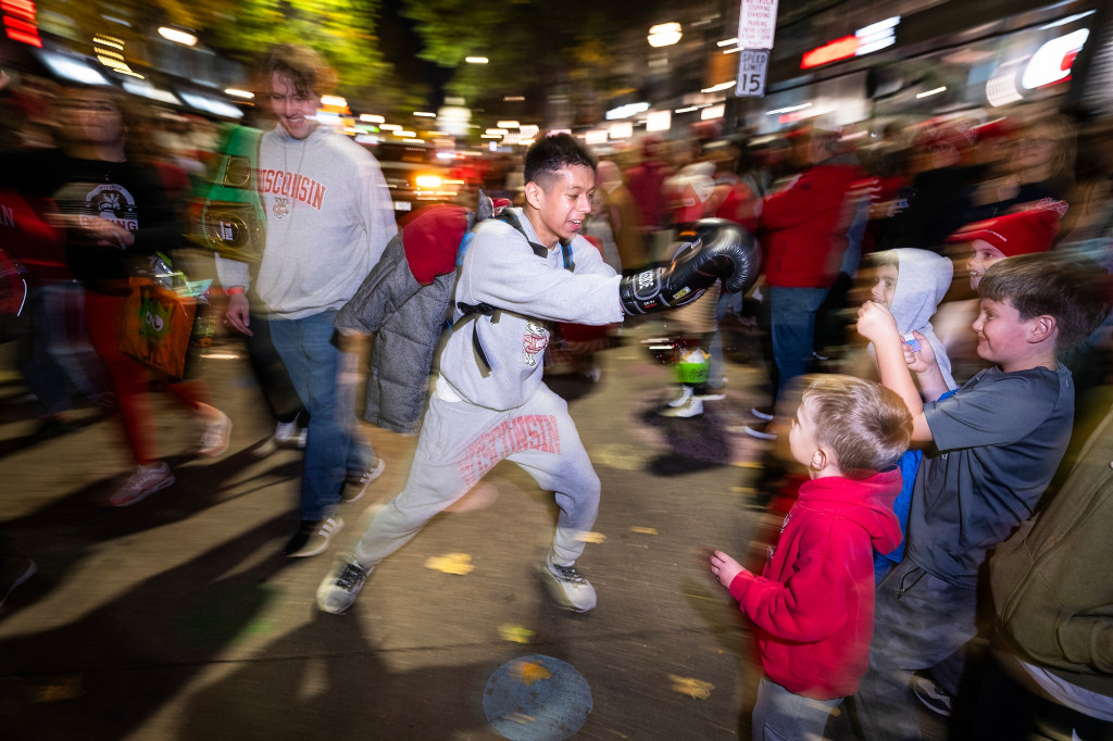 A person wear gray sweatpants and sweatshirt mocks throwing a punch at some kids.