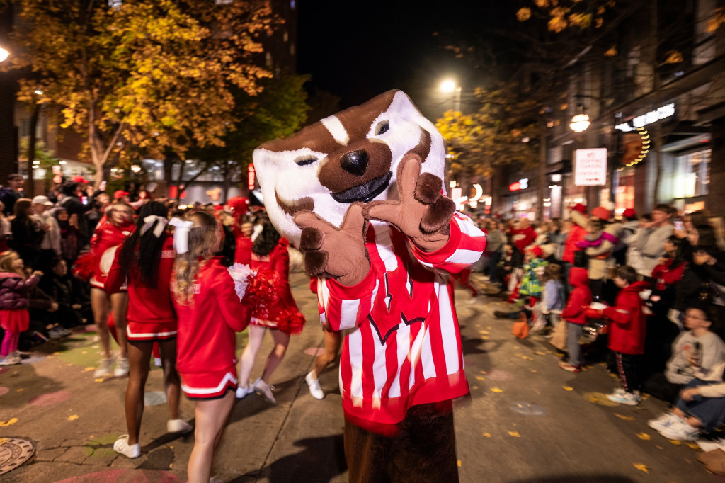 A person dressed up as Bucky Badger holds up his hands in a W sign as he's surrounded by excited Badger fans.