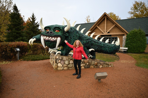 A woman poses in front of a statue of a dragon-like creature.