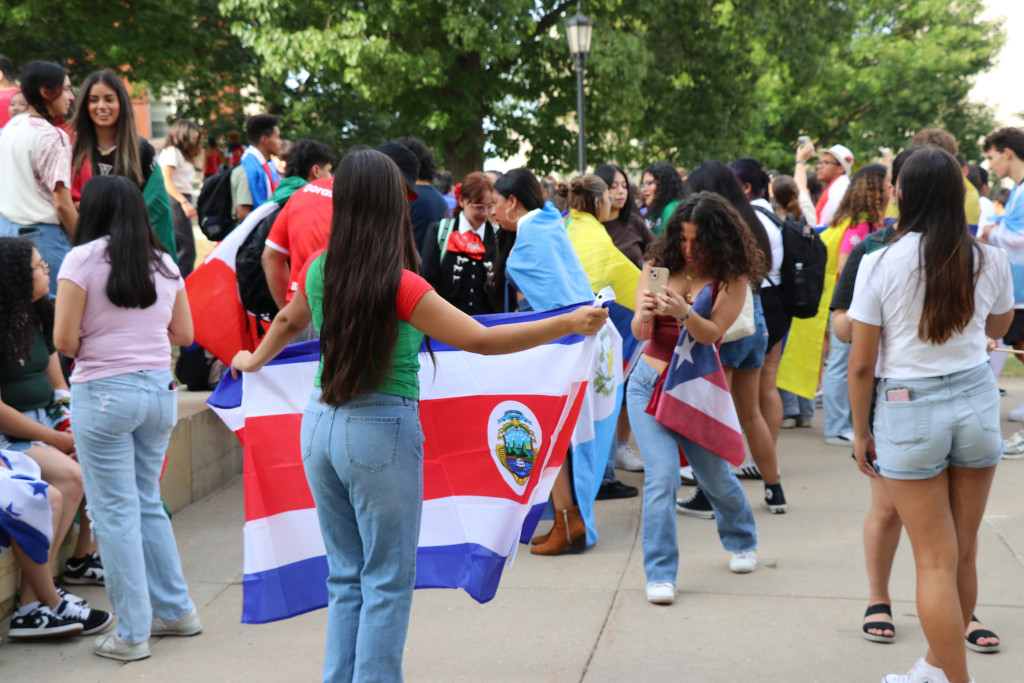 A student holds up a camera and takes a photo of another student who holds the Costa Rican flag.