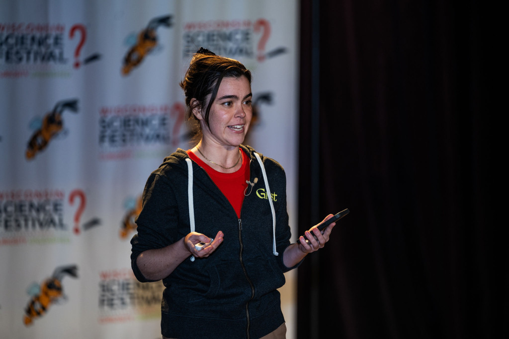 A woman is shown speaking and gesturing on stage.