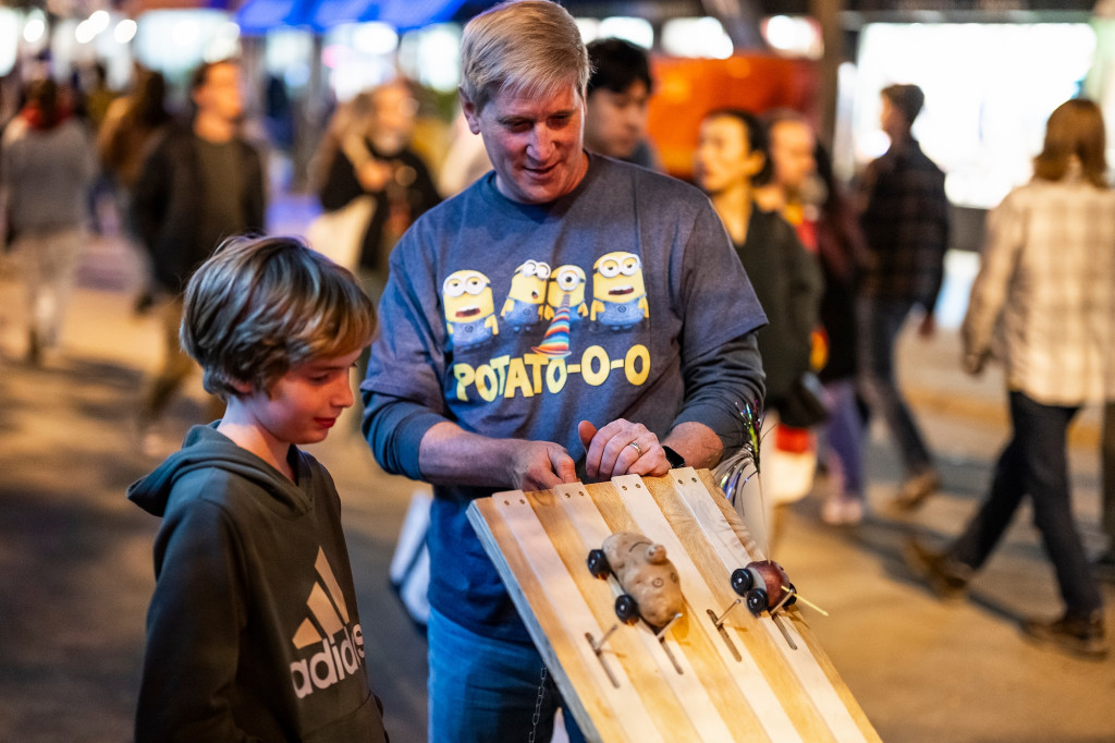 A man and a boy talk as a man prepares a racetrack for potatoes.