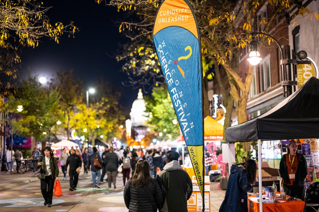 People walk along a street filled with booths at nighttime.