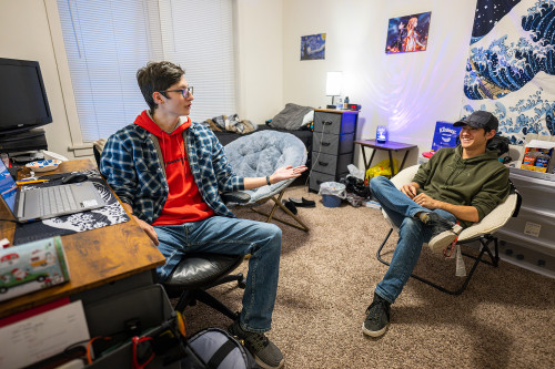 Two young men sitting in chairs gesticulate and talk.