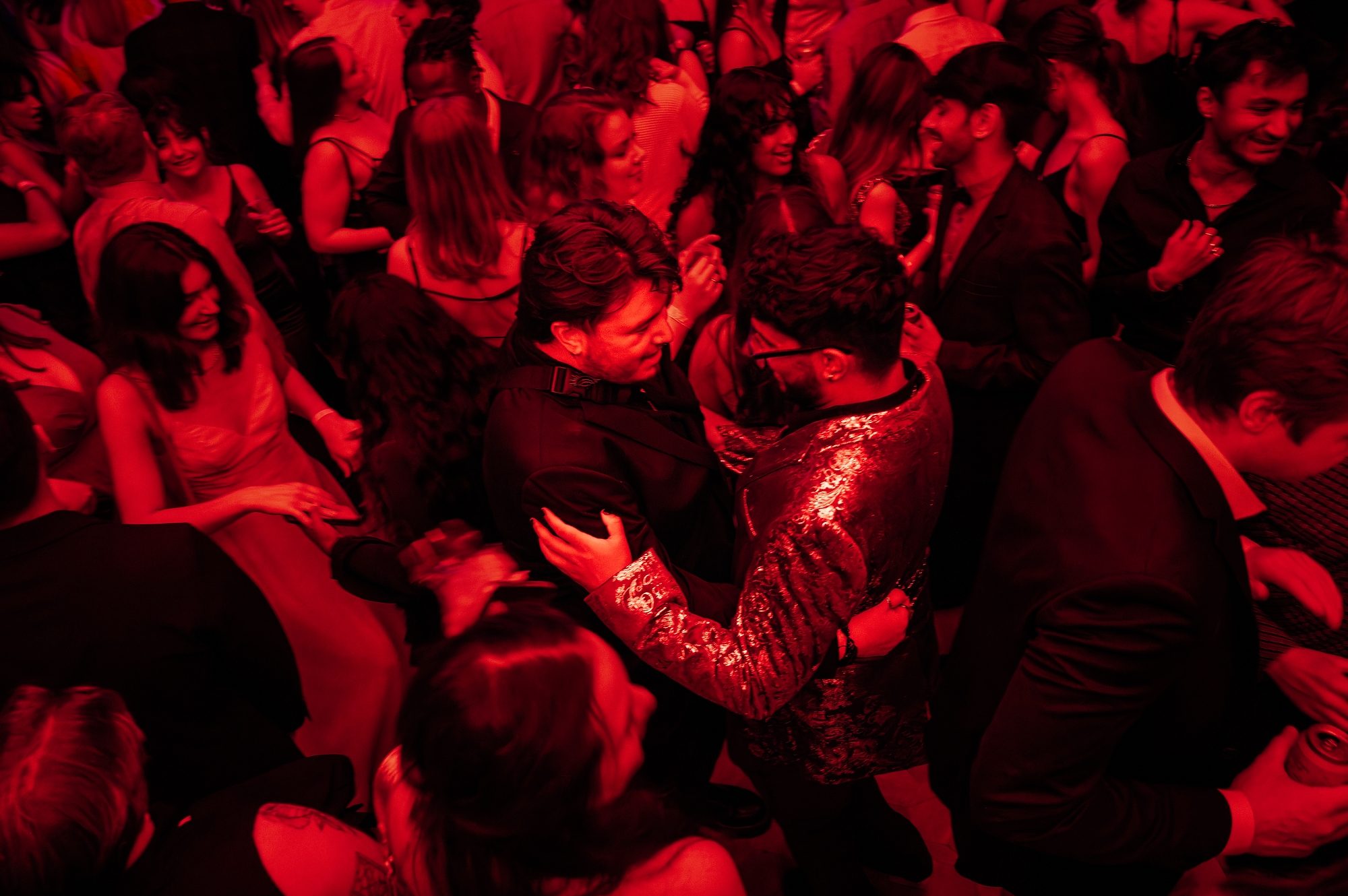 Image showing a lively party atmosphere with people dancing and socializing under red lighting.