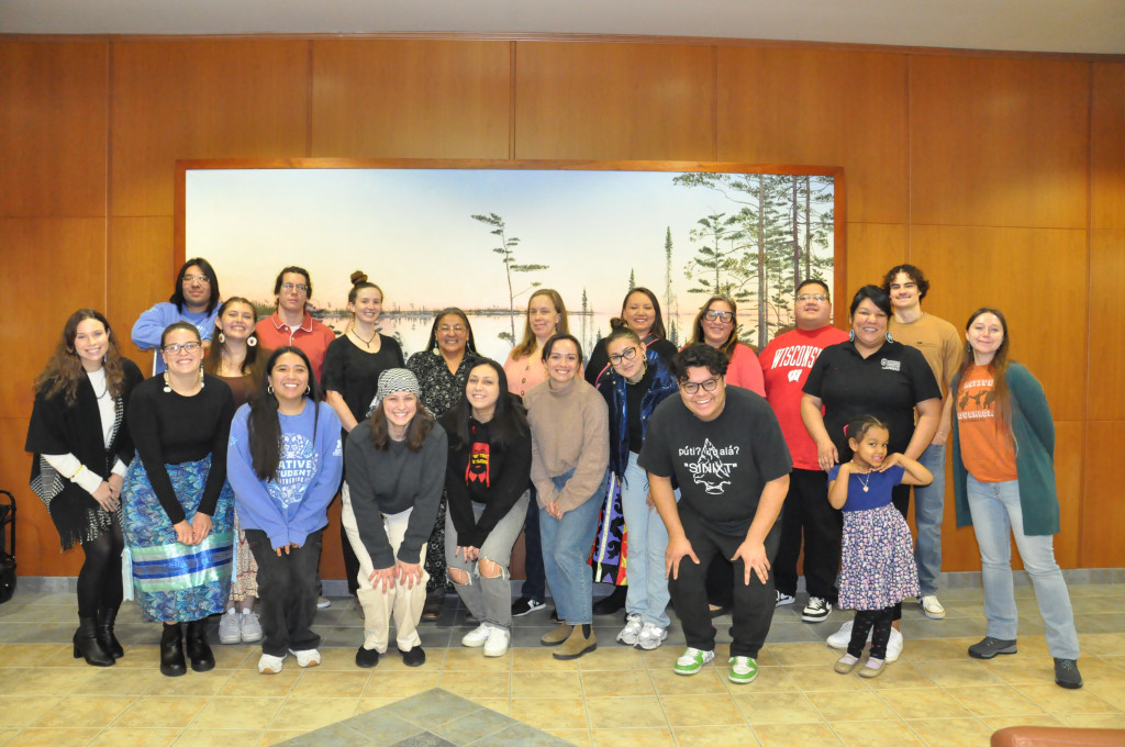 A group of Indigenous students and alumni gather in front of a mural and pose for a group photo. 