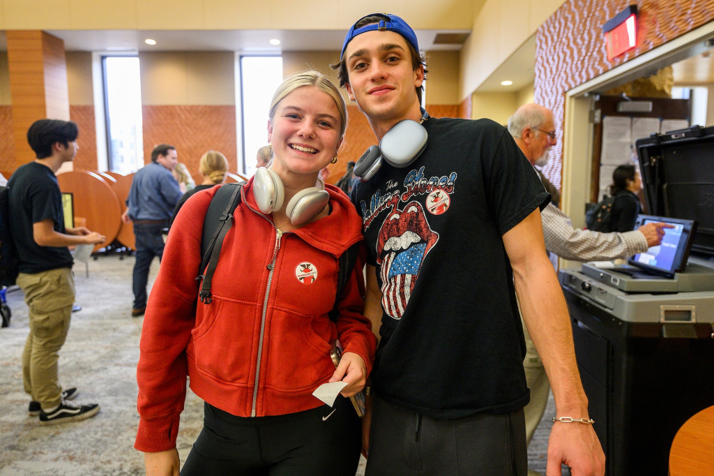 A young man and young woman are arm and arm, smiling for the camera. They wear 