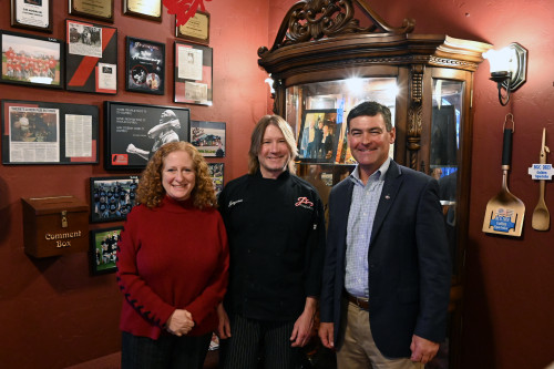 Three people standing in a tavern smile for the camera.