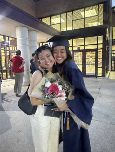 Two young women hug; one of them is wearing a commencement gown and cap.